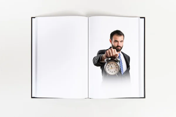 Молодой бизнесмен держит в руках старинные часы, напечатанные на книге — стоковое фото