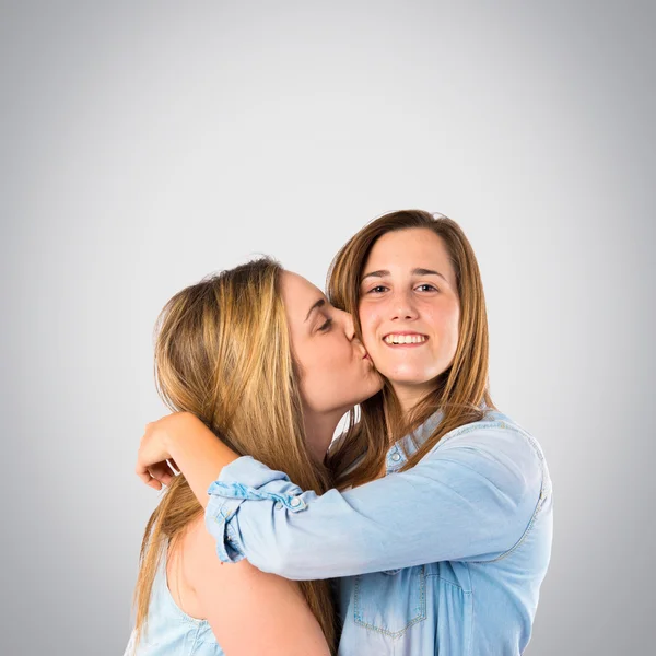 Girl giving kiss at her sister over grey background — Stock Photo, Image