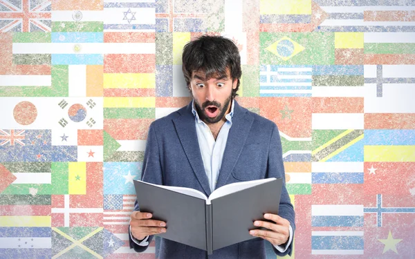 Surprised man reading a book over flags background — Stock Photo, Image