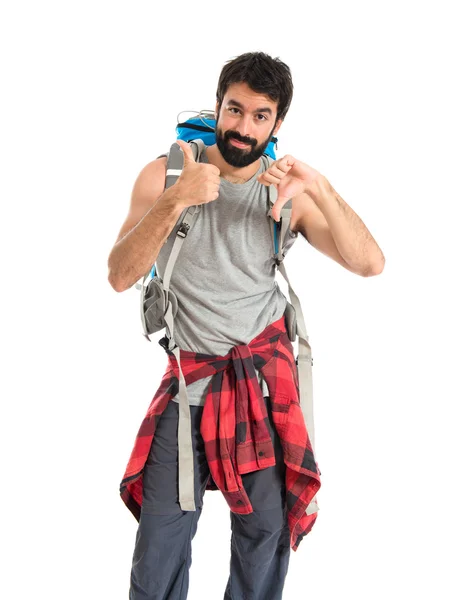 Backpacker making a good-bad sign over white background — Stockfoto