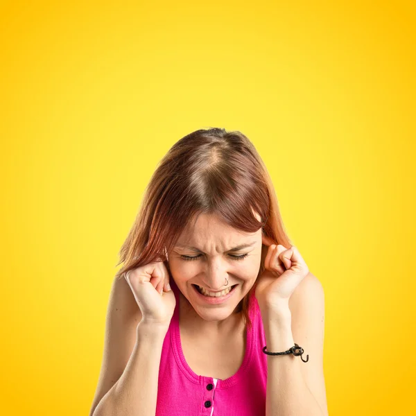 Jovencita cubriendo sus orejas sobre fondo amarillo — Foto de Stock