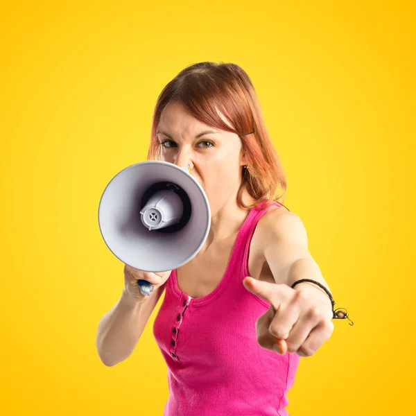 Рыжая девушка кричит с мегафоном на желтом фоне — стоковое фото
