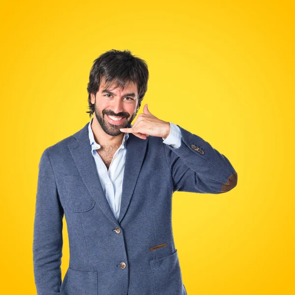 Businessman doing phone gesture over yellow background — Stock Photo, Image