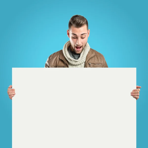 Handsome man holding an empty cardboard over blue background — Stock Photo, Image