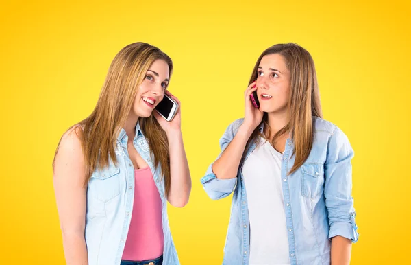 Unga tjejer pratar till mobila över gul bakgrund — Stockfoto