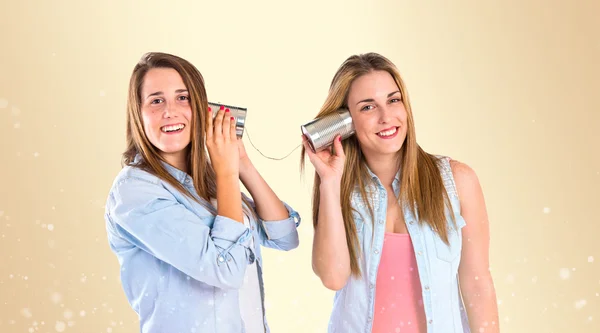 Amigos falando através de um telefone estanho sobre fundo amarelo — Fotografia de Stock