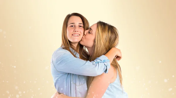 Chica dando beso a su hermana sobre fondo amarillo —  Fotos de Stock
