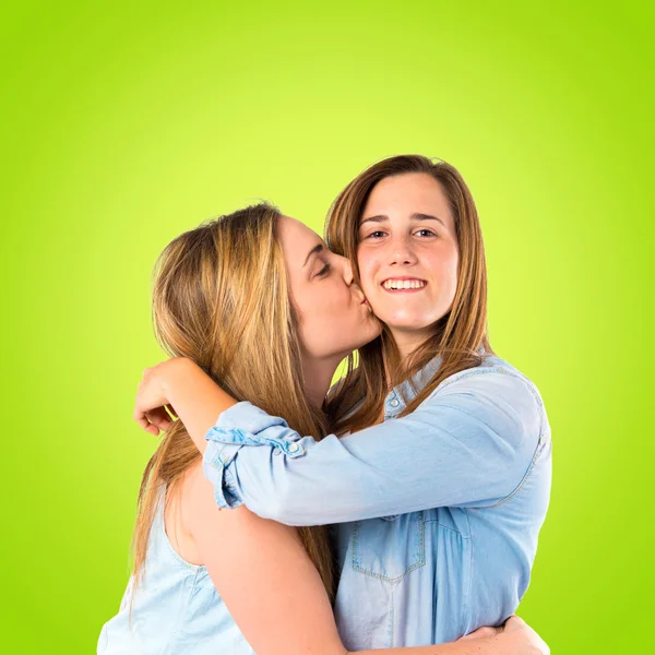 Girl giving kiss at her sister over green background — Stock Photo, Image