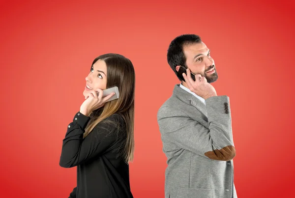 Couple talking to mobile over red background. — Stock Photo, Image