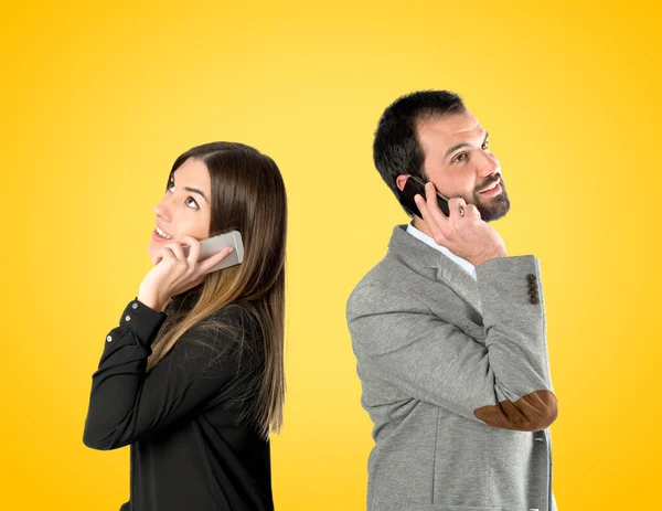 Couple talking to mobile over yellow background. — Stock Photo, Image