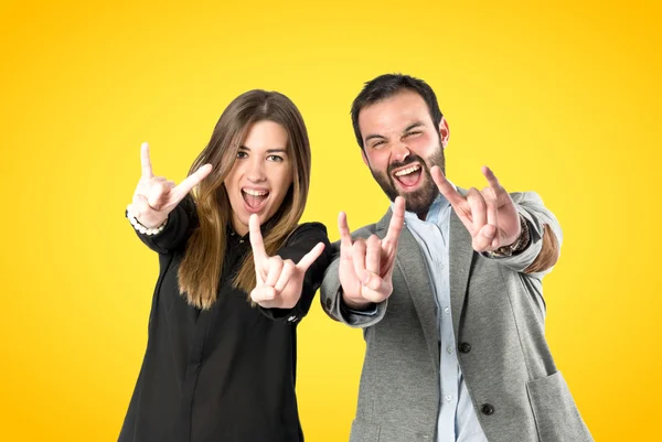 Casal fazendo o sinal de chifre sobre fundo amarelo — Fotografia de Stock