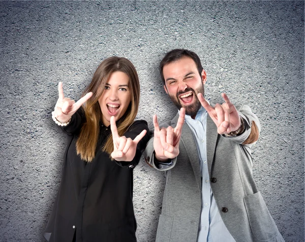 Couple doing the horn sign over textured background — Stock Photo, Image