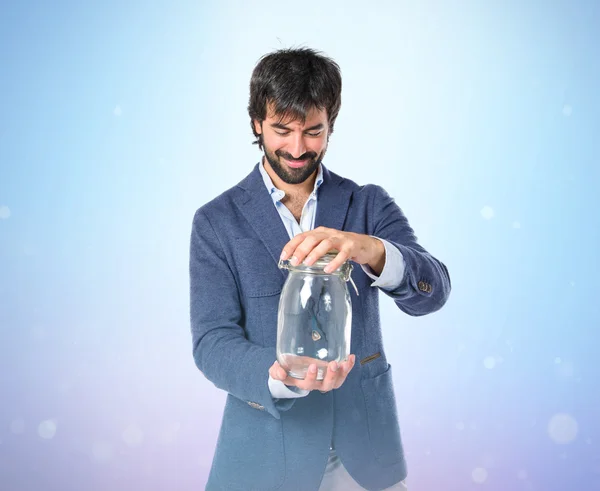 Handsome man holding an empty glass jar over blue background — Stock Photo, Image