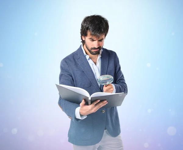 Uomo d'affari con loupe reding un libro su sfondo blu — Foto Stock