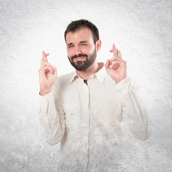 Jonge man met zijn vingers oversteken witte achtergrond — Stockfoto