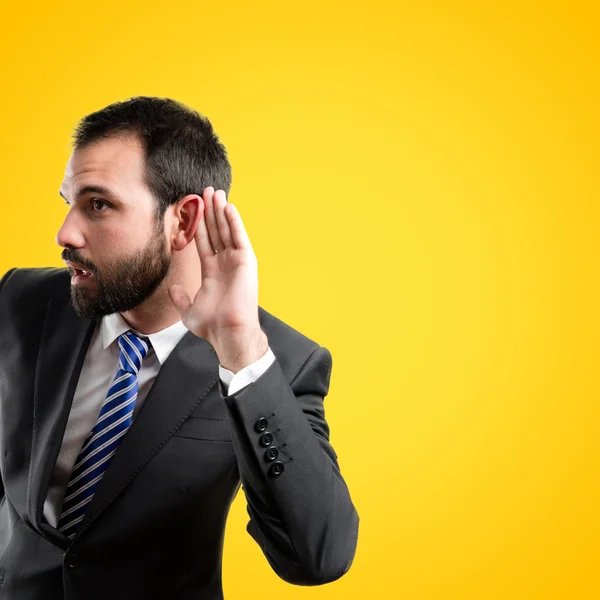 Young business man hearing something over yellow background — Stock Photo, Image