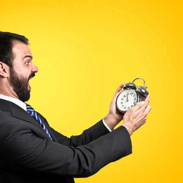 Молодой бизнесмен держит антикварные часы на желтом фоне — стоковое фото