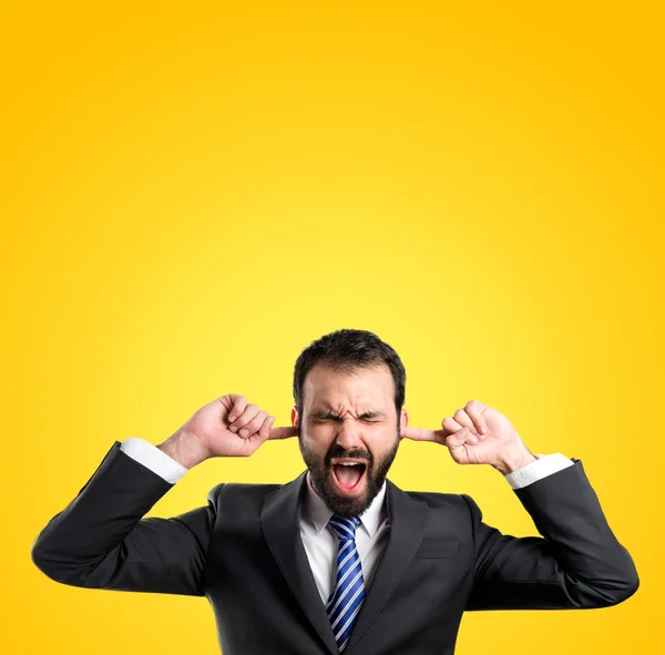 Business man covering her ears over yellow background — Stock Photo, Image