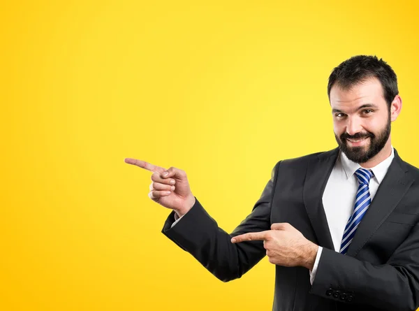 Businessman pointing to the side over yellow background — Stock Photo, Image