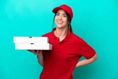 İş üniformalı pizzacı kadın, mavi arka planda izole edilmiş pizza kutularını alıyor. Kolları kalçasında poz veriyor ve gülümsüyor.