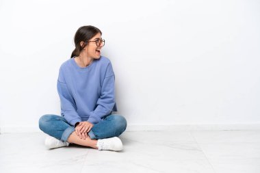 Beyaz arka planda izole bir şekilde yerde oturan beyaz bir kadın yan yana gülüyor.