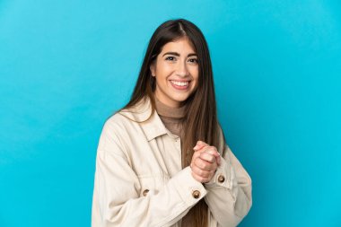 Mavi arka planda izole edilmiş genç beyaz kadın gülüyor.