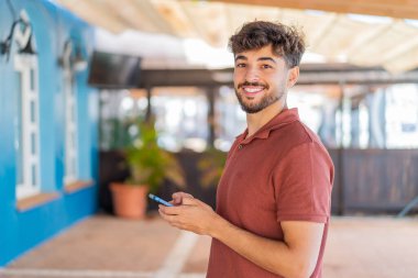 Dışarıdaki yakışıklı genç Arap adam cep telefonuyla mesaj ya da e-posta yolluyor.