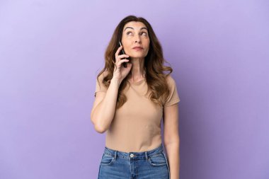 Orta yaşlı beyaz kadın cep telefonu kullanıyor. Mor arka planda izole edilmiş ve yukarı bakıyor.