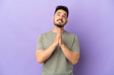 Mor arka planda izole edilmiş genç beyaz adam avuç içlerini bir arada tutuyor. İnsan bir şey ister.