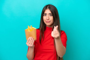 Mavi arka planda izole edilmiş patates kızartması yakalayan beyaz bir kadın para hareketi yapıyor.