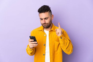 Beyaz adam mor arka planda cep telefonu ve parmak kaldırarak izole edilmiş.