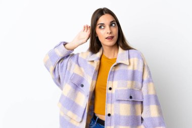 Mor arka planda izole edilmiş genç beyaz kadın elini kulağına koyarak bir şeyler dinliyor.