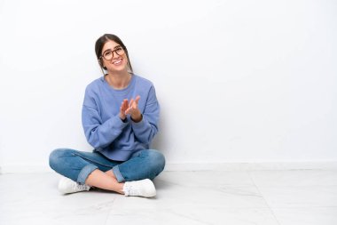 Beyaz arka planda izole bir şekilde yerde oturan beyaz bir kadın bir konferansta sunumdan sonra alkışlıyor.