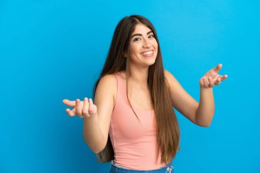 Mavi arka planda izole edilmiş genç beyaz kadın mutlu ve gülümsüyor.