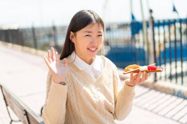 Genç Çinli bir kadın açık havada sashimi tutuyor ve mutlu bir ifadeyle selamlıyor.