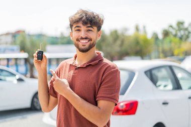 Genç Arap yakışıklı adam arabanın anahtarını açık havada tutuyor ve ona doğrultuyor.