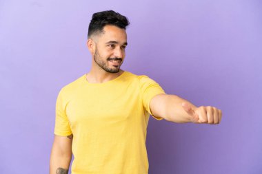 Mor arka planda izole edilmiş genç beyaz bir adam baş parmak hareketi yapıyor.