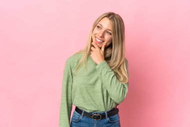 Pembe arka planda soyutlanmış genç sarışın kadın yan bakıyor ve gülümsüyor.