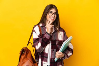 Sarı arka planda izole edilmiş genç bir bayan gülümseyerek yukarı bakıyor.