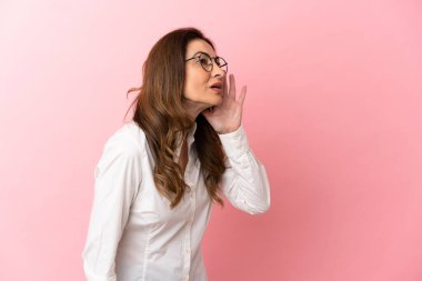 Pembe arka planda izole edilmiş orta yaşlı beyaz kadın ağzı sonuna kadar açık bağırıyor.