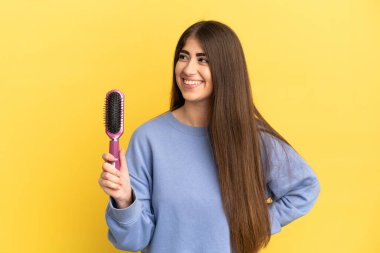 Mavi arka planda saç fırçası tutan beyaz bir kadın.