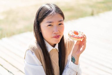 Dışarıdaki genç Çinli kadın elinde donut tutuyor.