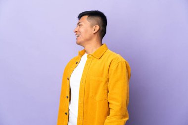 Genç Ekvadorlu adam, mor arka planda izole edilmiş. Yan pozisyonda gülüyor.