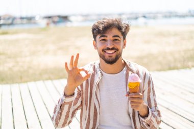 Açık havada kornet dondurması olan yakışıklı bir Arap, parmaklarıyla işaret veriyor.