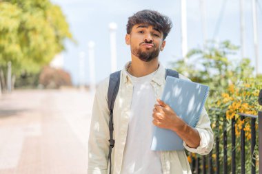 Genç bir Arap öğrenci dışarıda üzgün bir ifadeyle bekliyor.