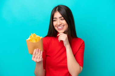 Mavi arka planda izole edilmiş patates kızartması yakalayan beyaz bir kadın yan tarafa bakıyor ve gülümsüyor.