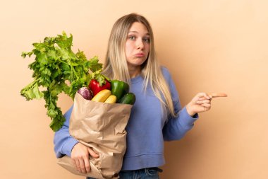 Elinde sebzelerle dolu bir çantayla gezen genç sarışın kadın yan taraftakilerin şüpheye düştüğünü gösteriyor.