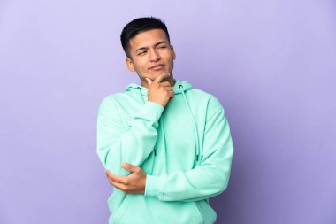 Genç Ekvadorlu adam mor arka planda izole edilmiş, yana bakıyor ve gülümsüyor.