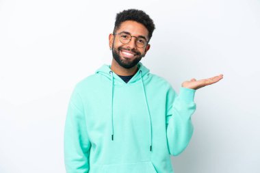 Beyaz arka planda izole edilmiş genç Brezilyalı bir adam bir ilan vermek için avucunun içinde hayali bir mekan tutuyor.