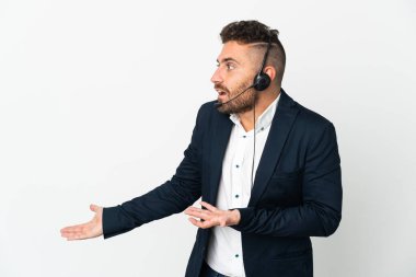 Tele-pazarlamacı beyaz arka planda izole edilmiş bir kulaklıkla çalışırken sürpriz bir ifadeyle yan tarafa bakıyor.